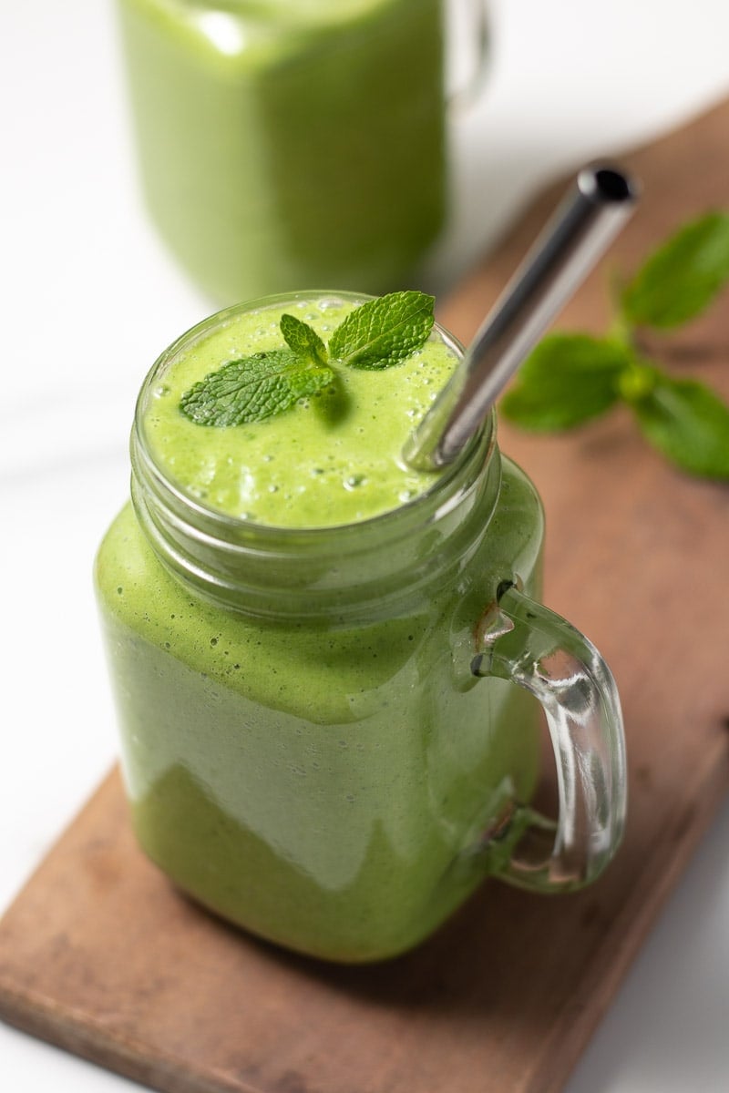 Green keto smoothie in a glass with a straw and garnished with mint