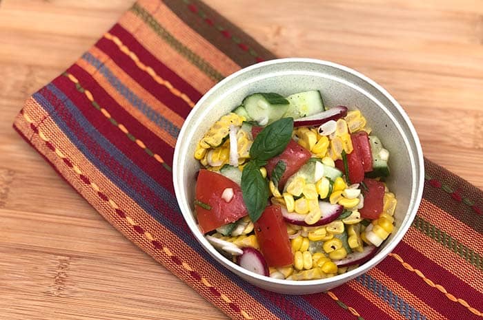 Summer Corn Salad with Basil Vinaigrette in a grey bowl on top of a decorative napkin, garnished with fresh basil leaves