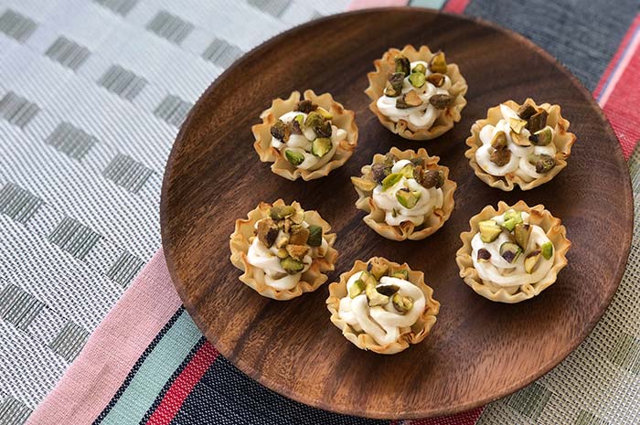 Seven Goat Cheese Bites with Pistachios on a round wooden serving tray.