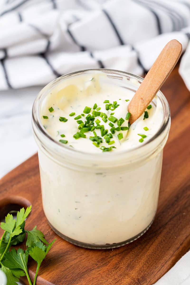 Finished ranch dressing in a glass jar with a wood spoon and garnished with fresh chives
