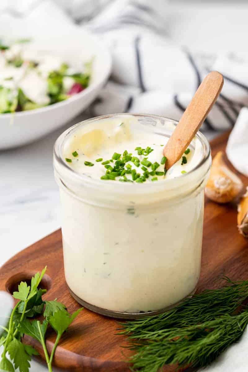 Keto ranch dressing in a small glass jar with a wooden spoon, garnished with fresh chives