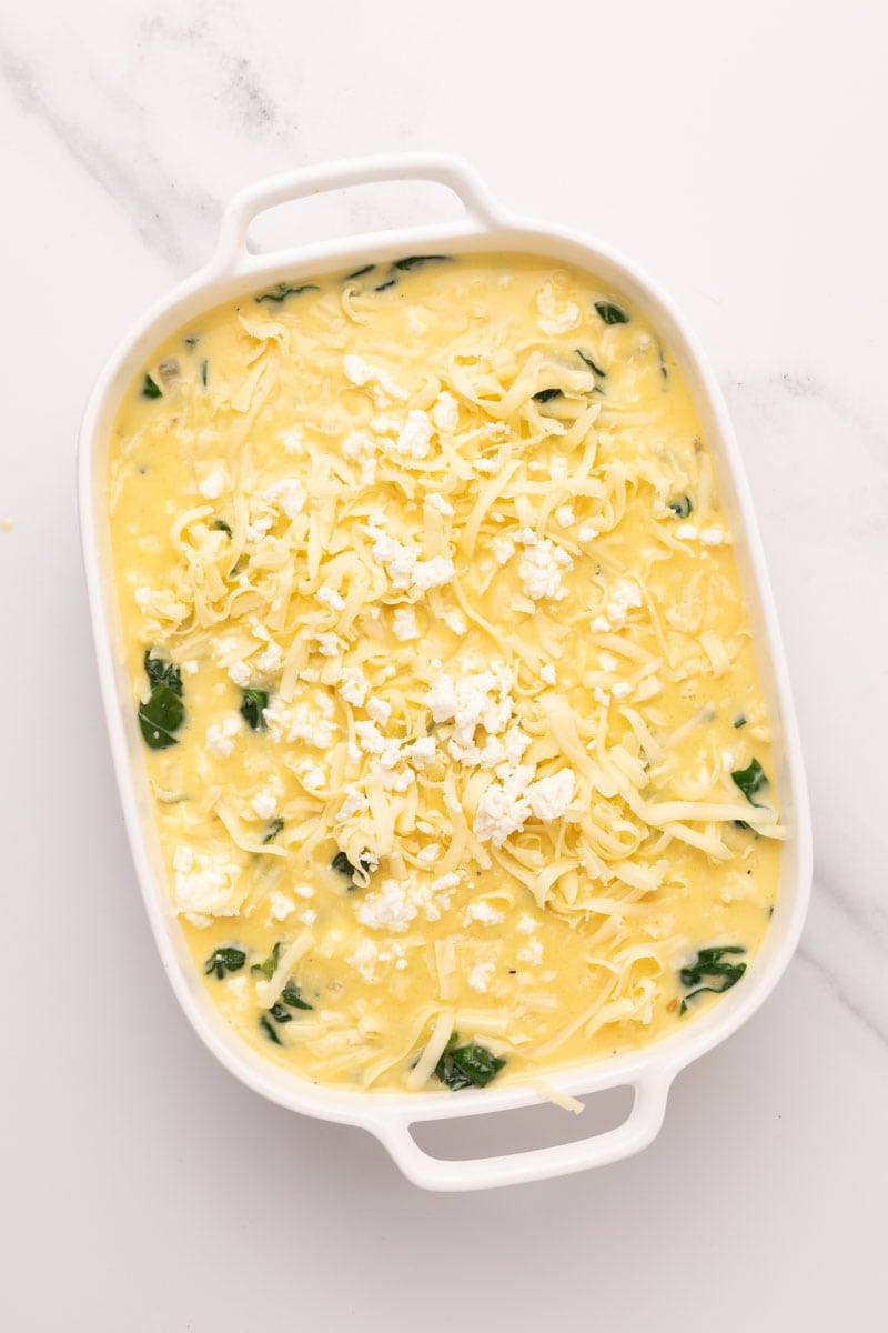 Uncooked egg bake in a casserole dish with cheese on top