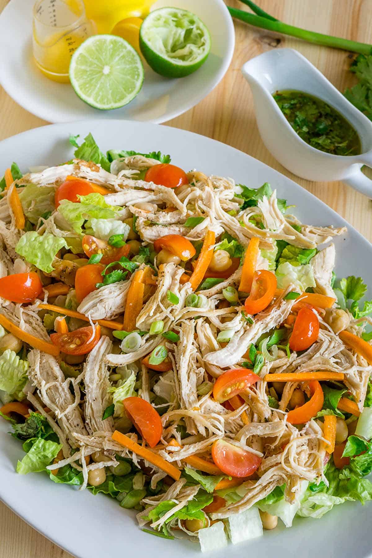 Plate of shredded chicken salad on a table with dressing on the side