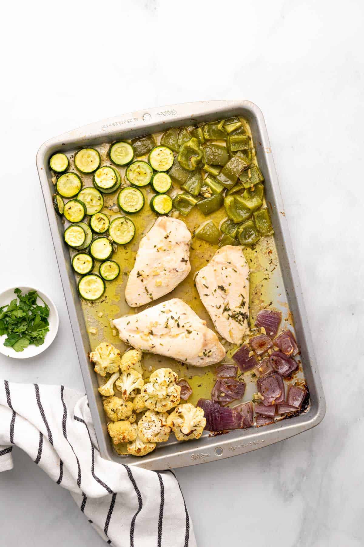 baked chicken and vegetables on a baking sheet with fresh herbs