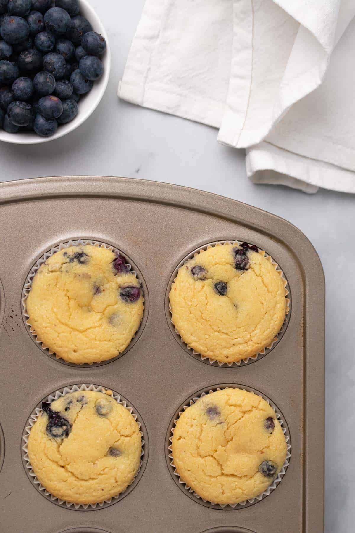 Close-up of blueberry muffins in a pan next to a ramekin of fresh blueberries