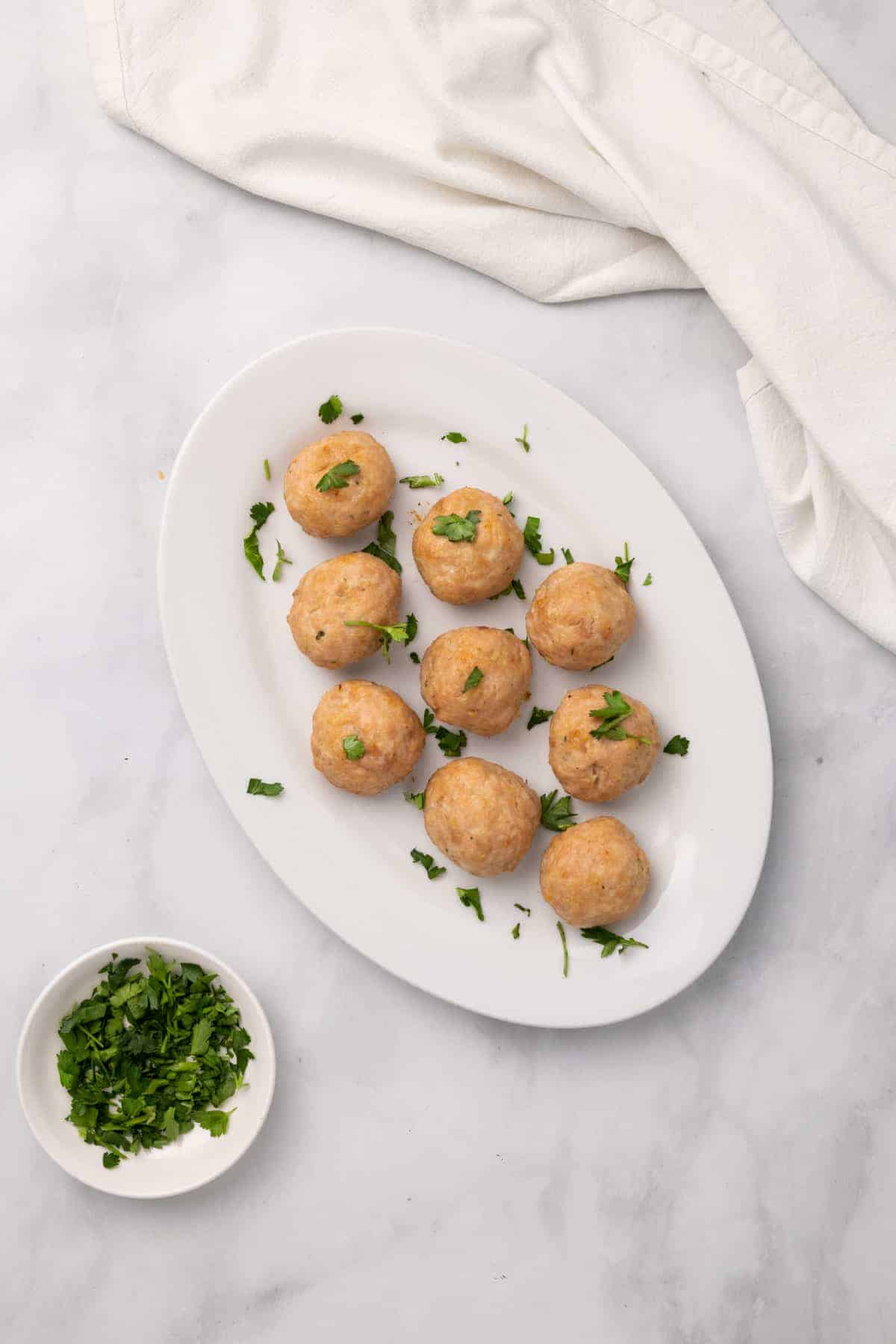 Meatballs on a white serving platter, garnished with fresh parsley, as seen from above