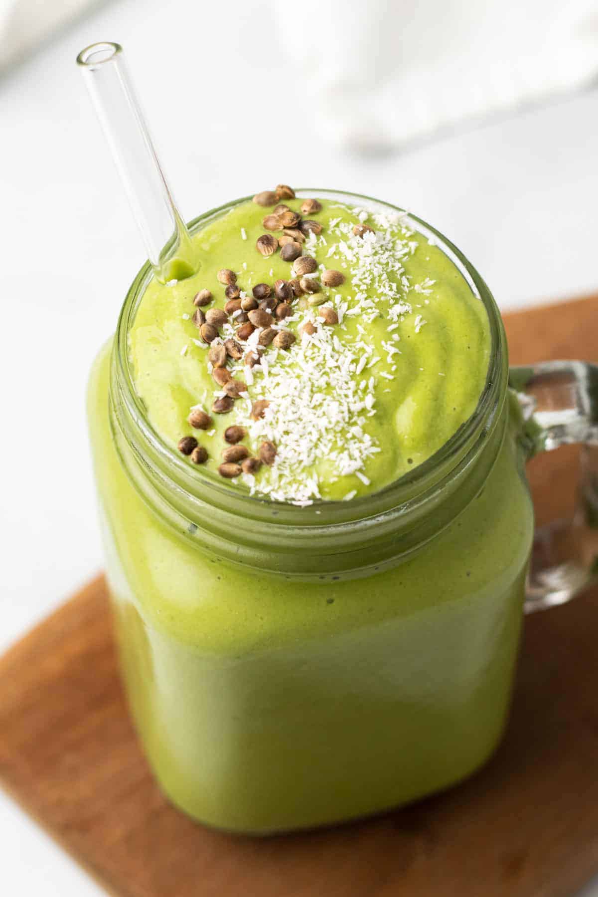 Low-Carb Green Smoothie in a glass jar with a glass straw and topped with shredded coconut and flax seeds