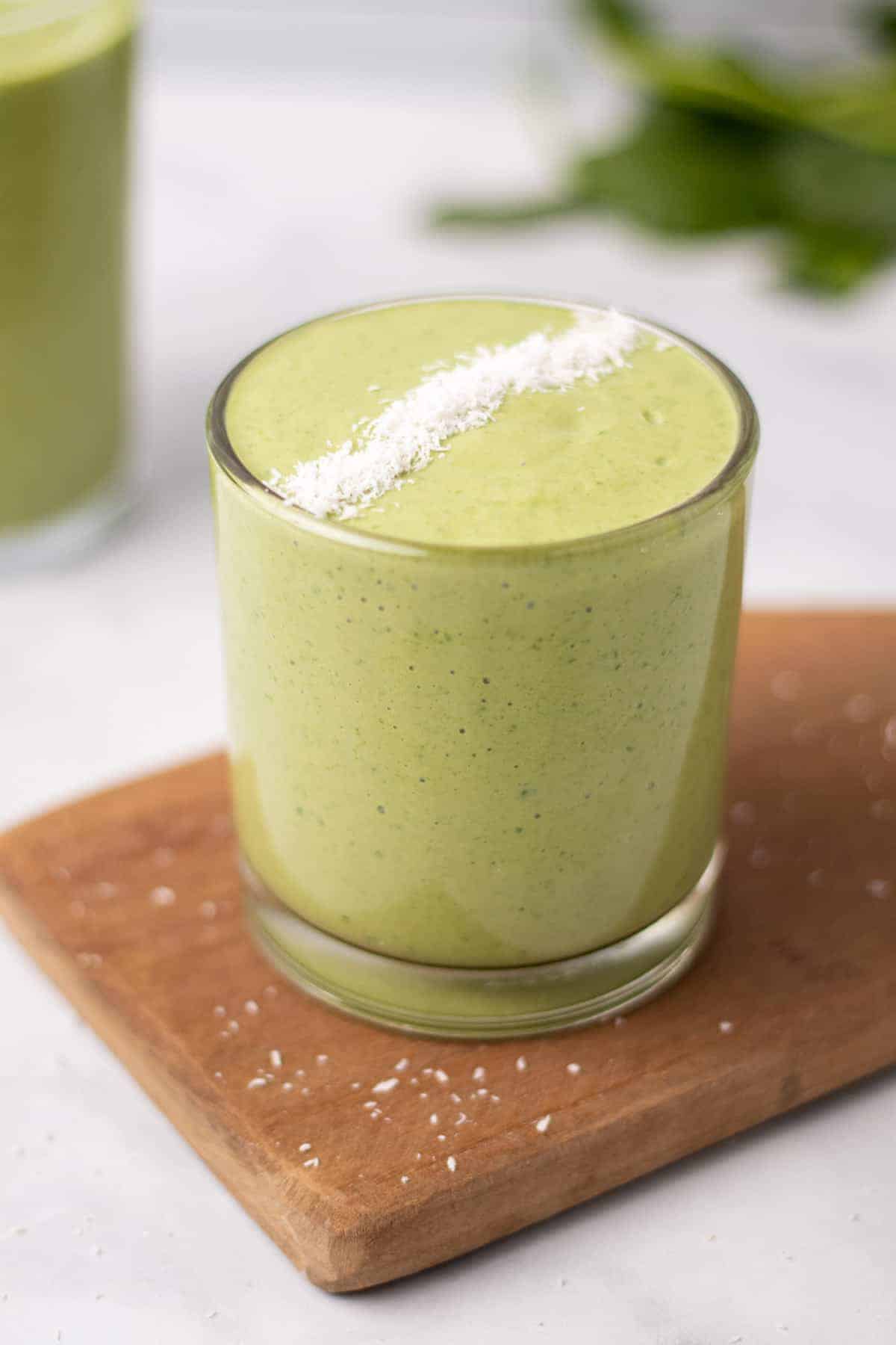 Spinach smoothie topped with finely shredded coconut in a glass on a wooden cutting board