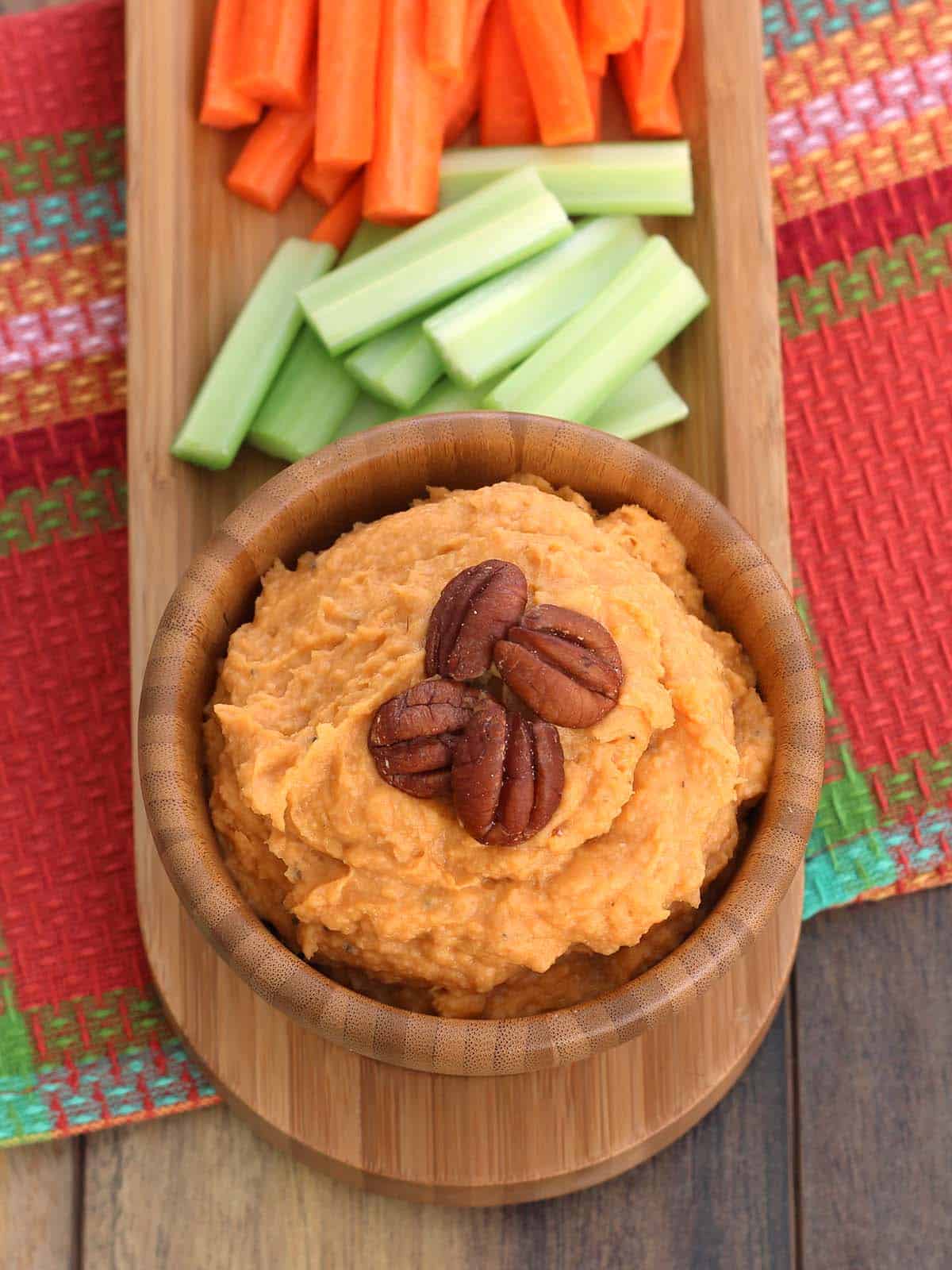 Sweet Potato Bean Dip in a wood bowl on a wood serving platter with carrot and celery sticks