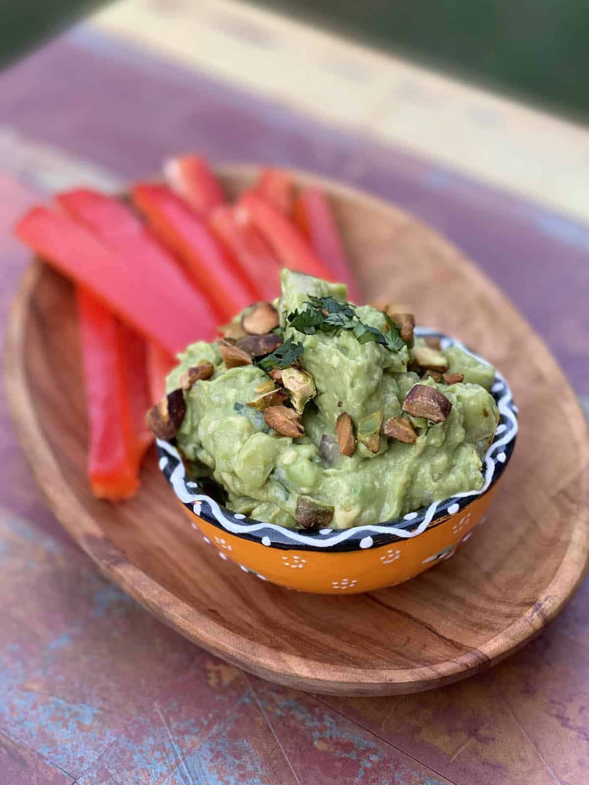 Pear Guacamole with Pistachios in a ramekin on a wooden serving tray with sliced red bell peppers