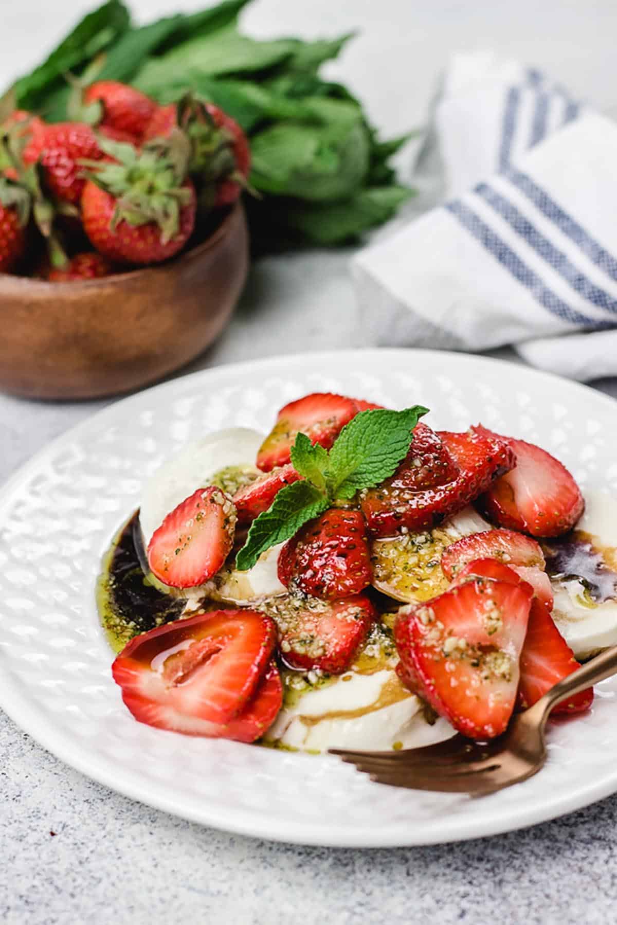 Strawberries and Fresh Mozzarella with Mint Pesto Drizzle on a white plate with a gold fork. 