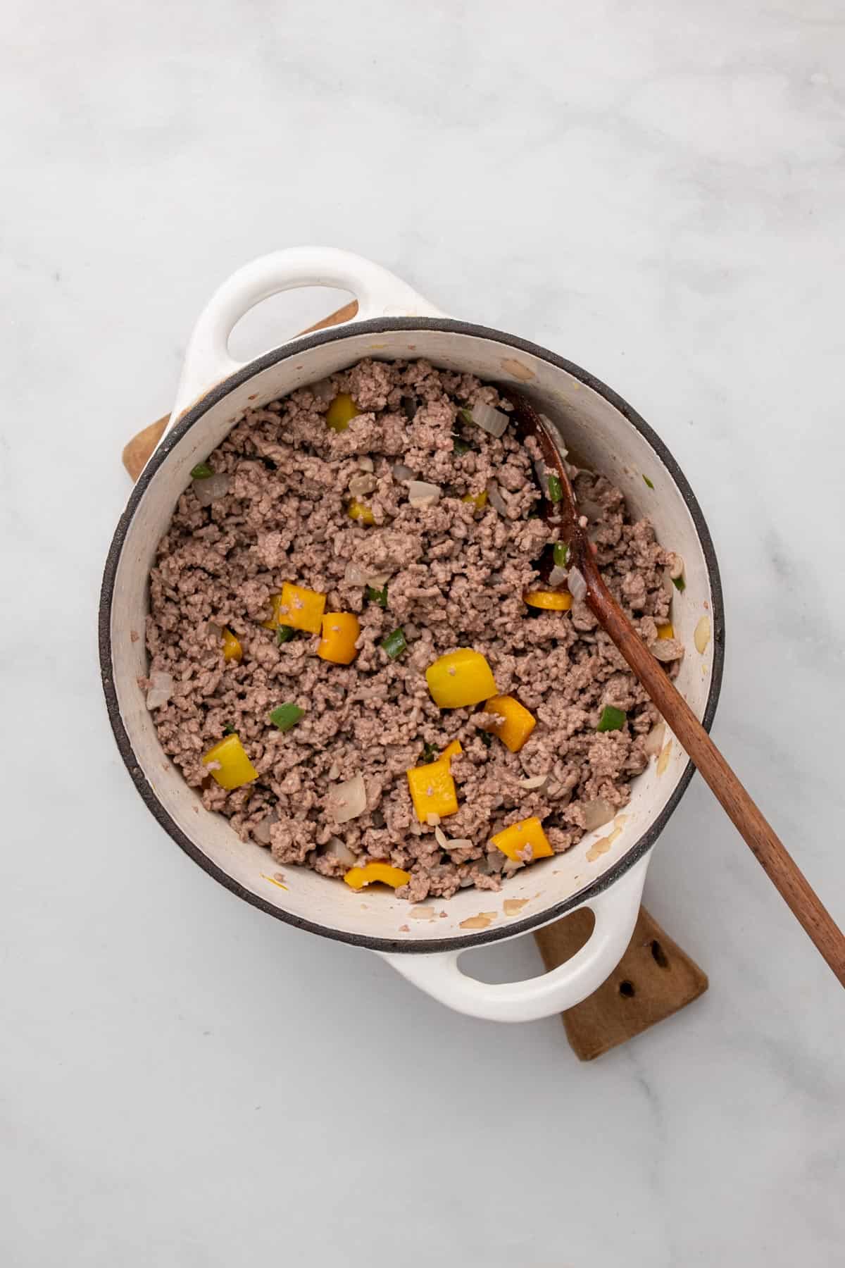 Cooked ground beef, onion, bell pepper, and green chilis in a white pot with a wooden spoon
