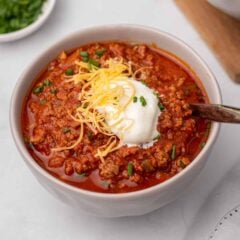Beanless chili in a white bowl topped with sour cream, shredded cheese, and green onion