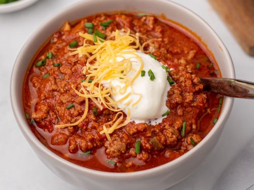 Beanless chili in a white bowl topped with sour cream, shredded cheese, and green onion