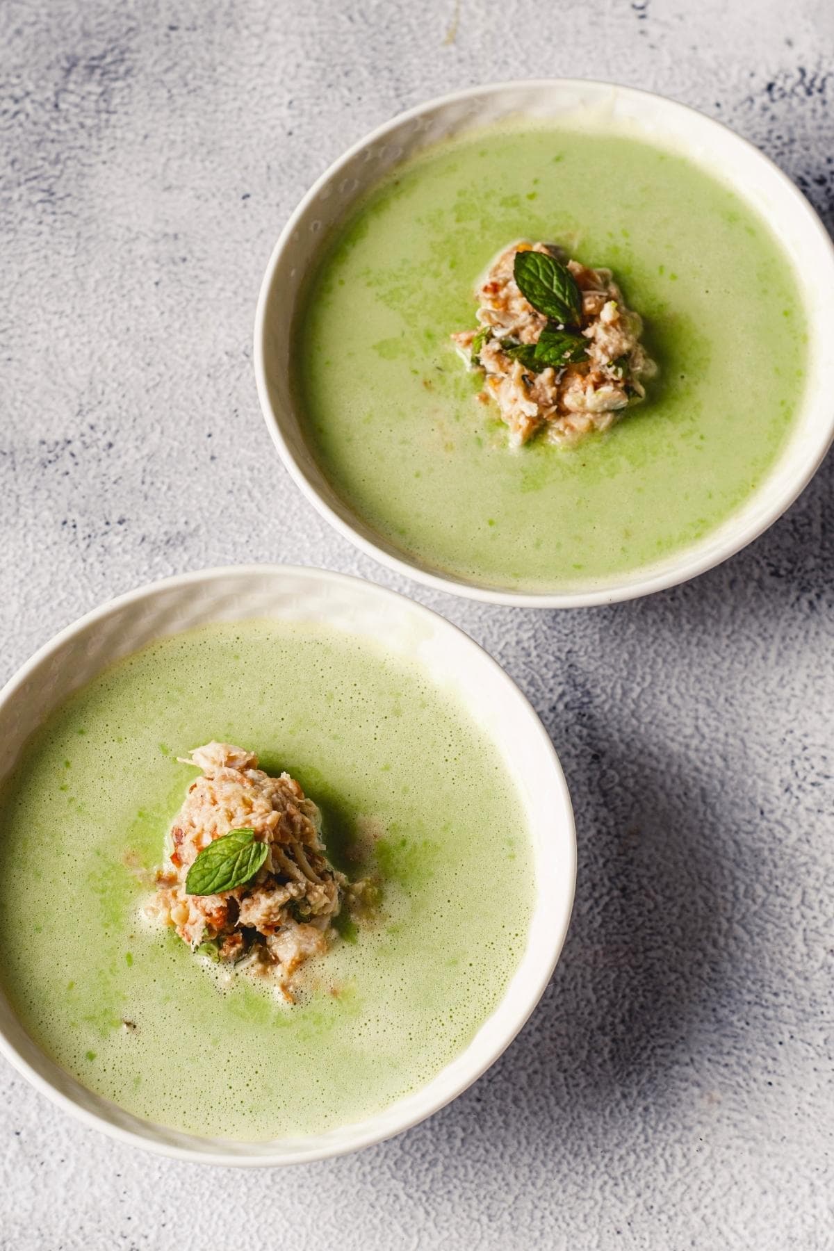 Two bowls of Cold Pea Soup with Crab and Mint on a table