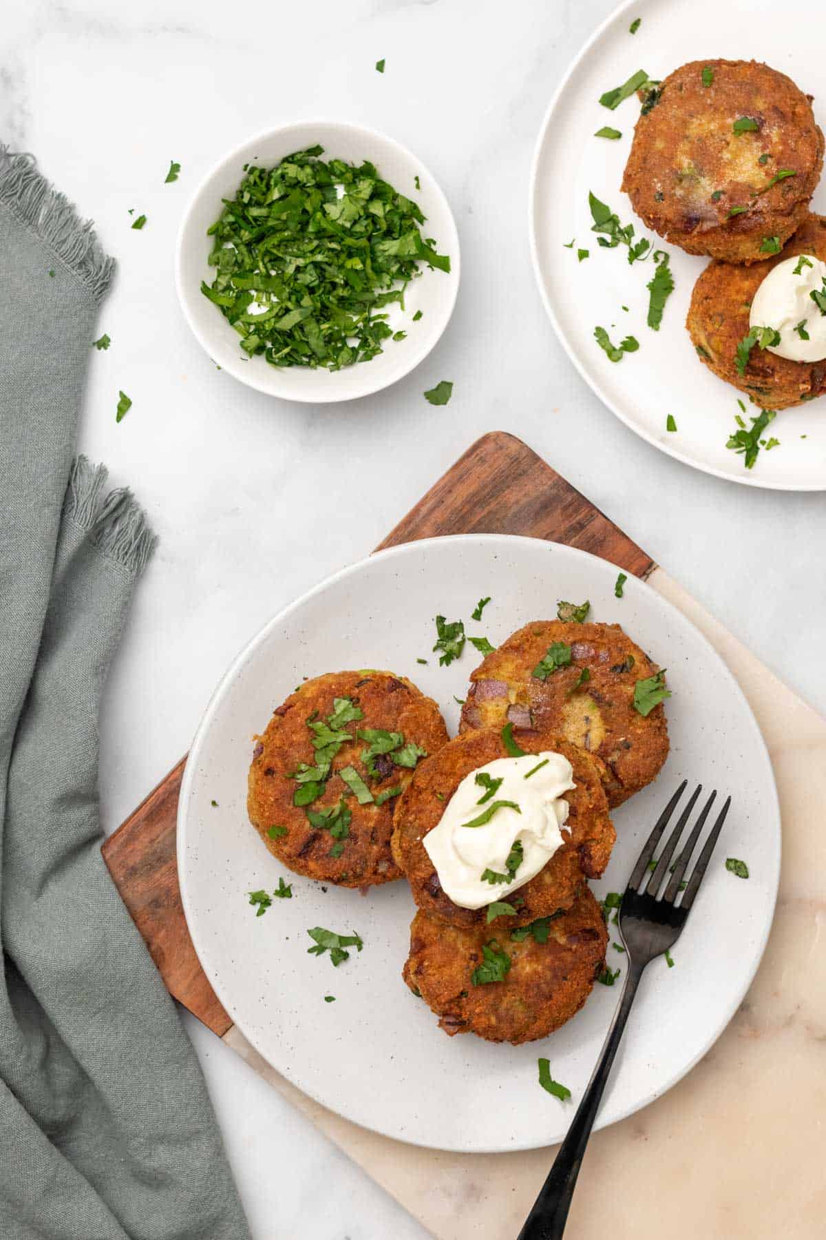 Salmon patties on white plates topped with parsley and sour cream