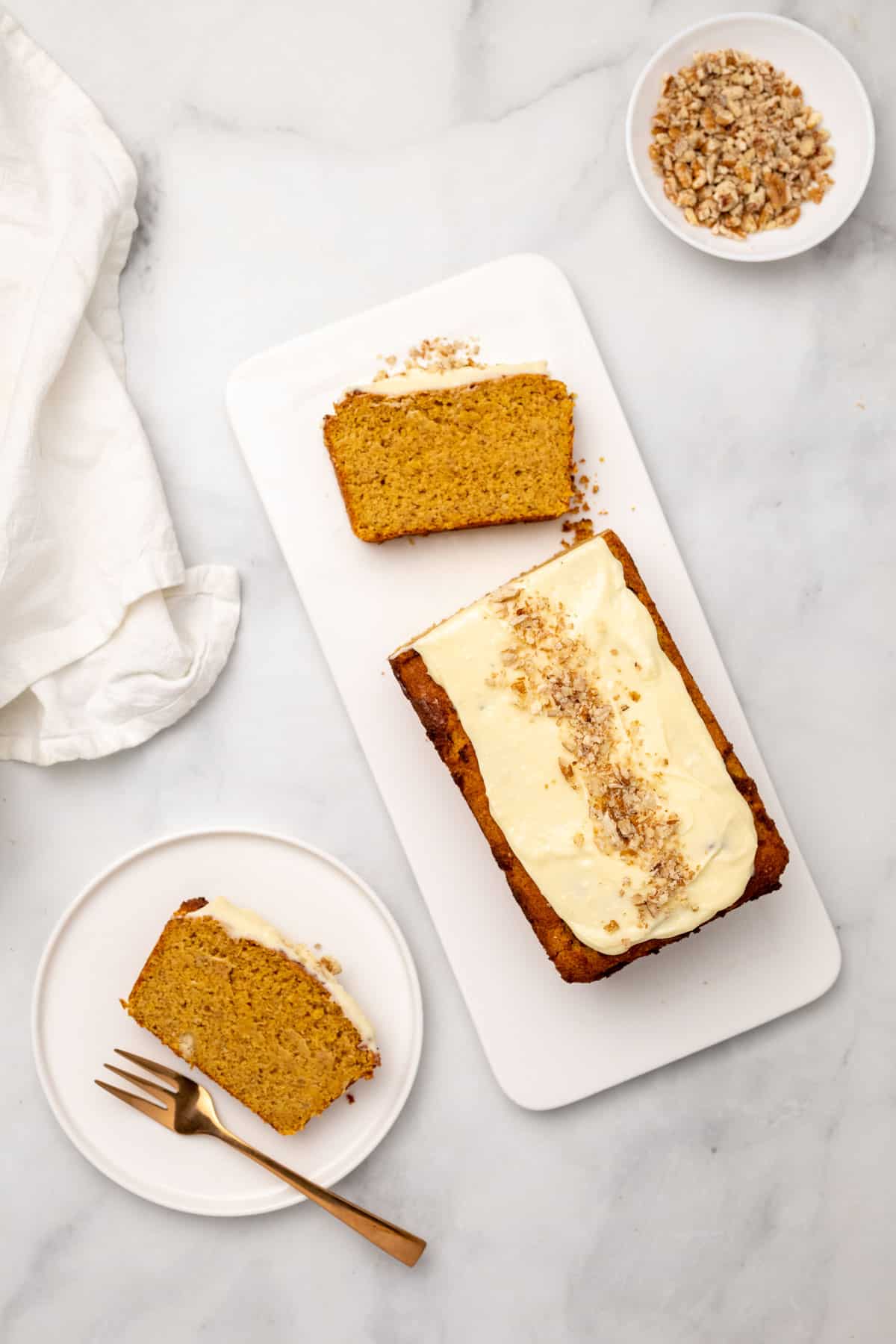 Pumpkin loaf on a serving tray next to a plate with a slice and a bowl for chopped nuts