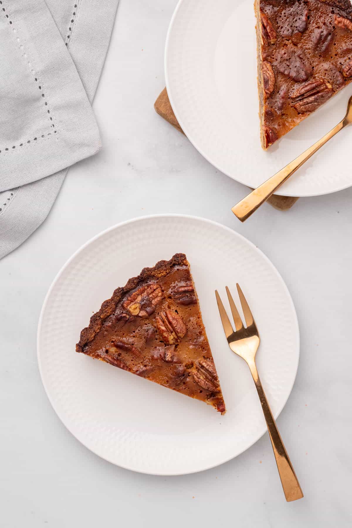 Two slices of pecan pie on white plates with gold forks, as seen from above