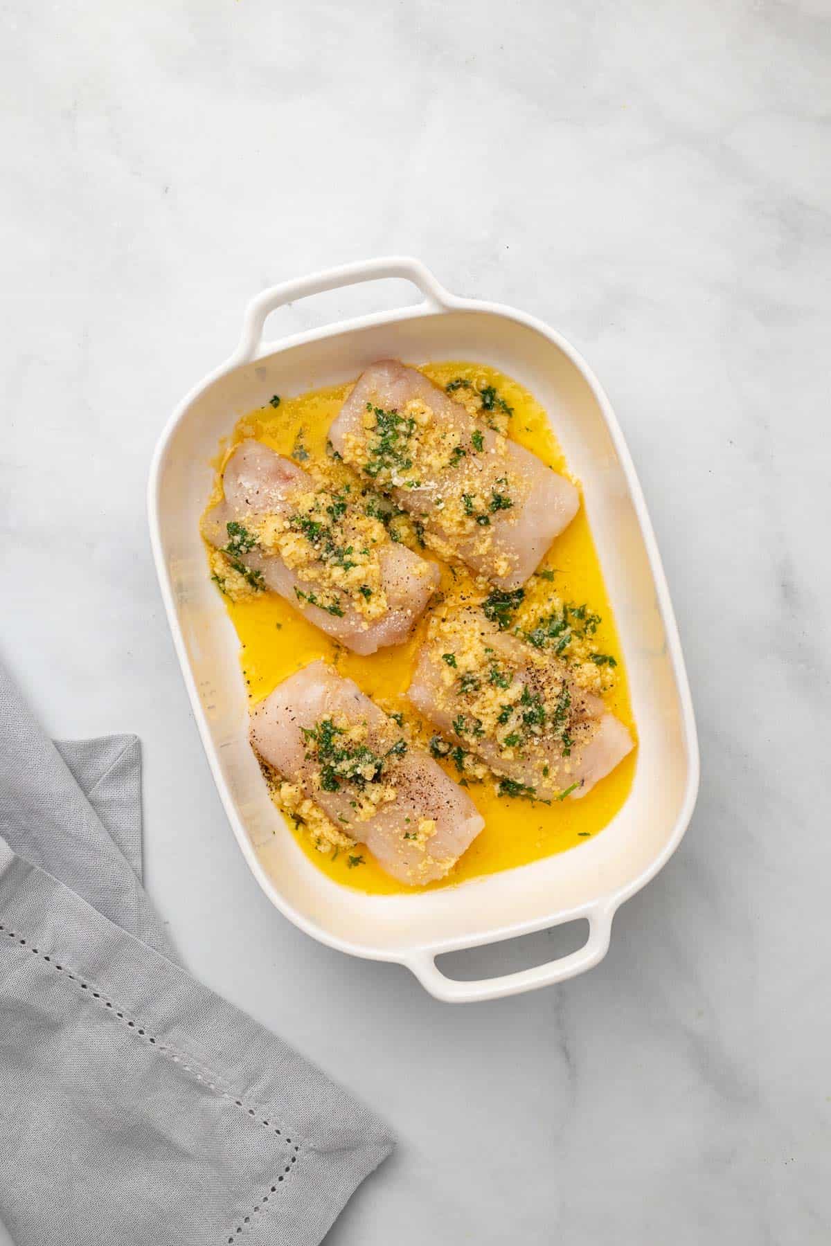 Cod filets in the baking dish with butter, garlic, parmesan, and parsley