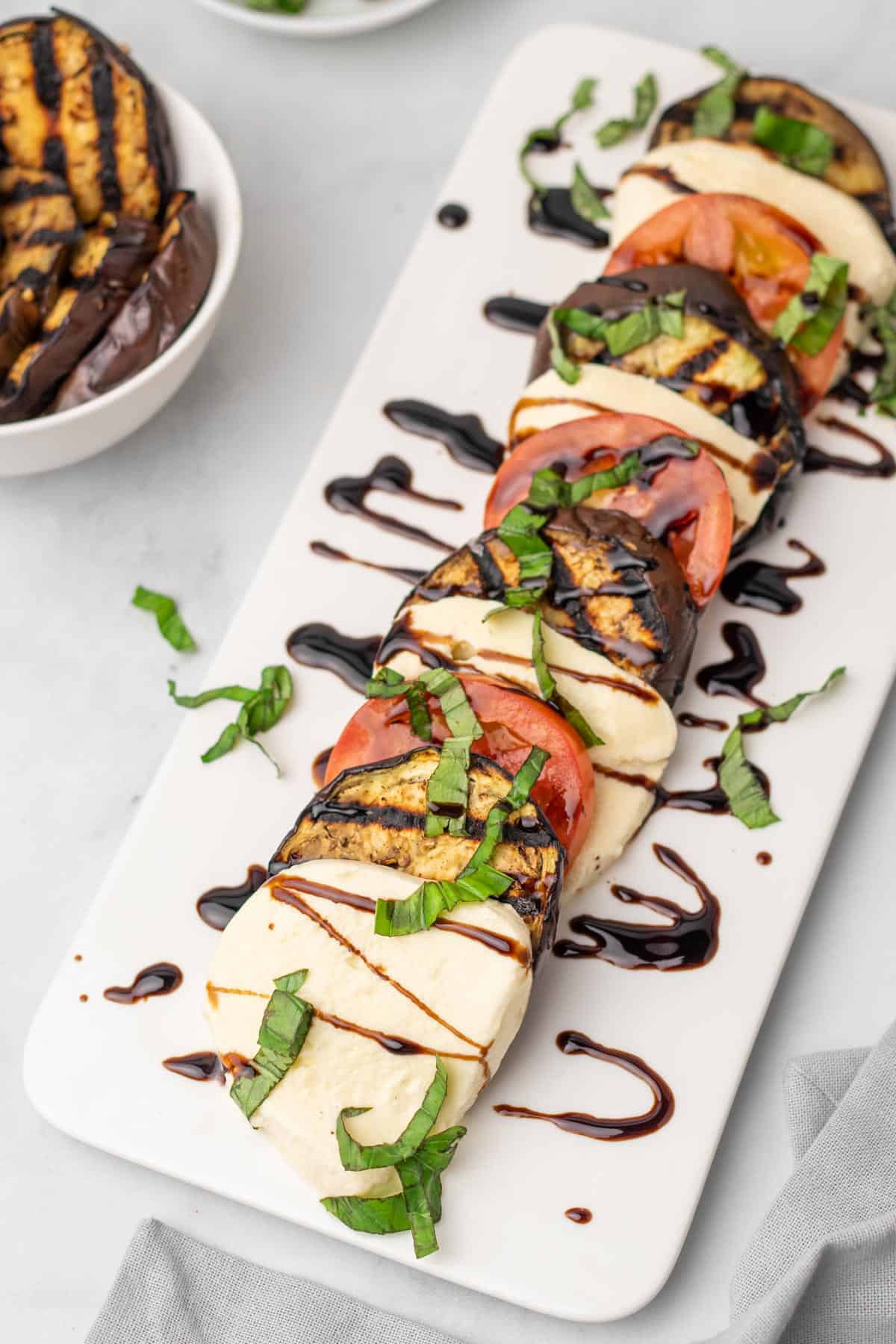 Eggplant caprese salad on a white serving dish garnished with balsamic and fresh cut basil