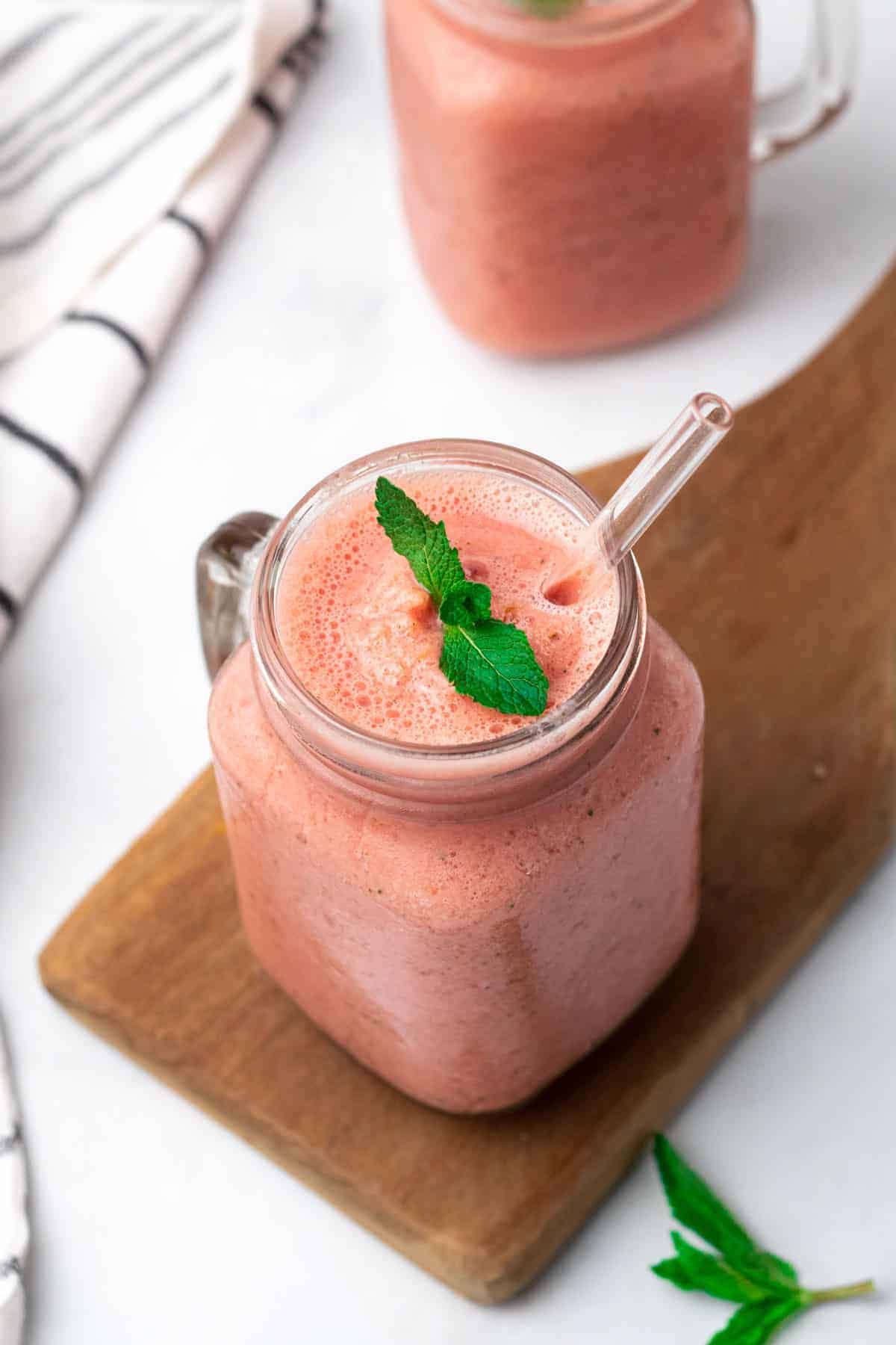 Smoothie in a glass jar with a straw, garnished with fresh mint