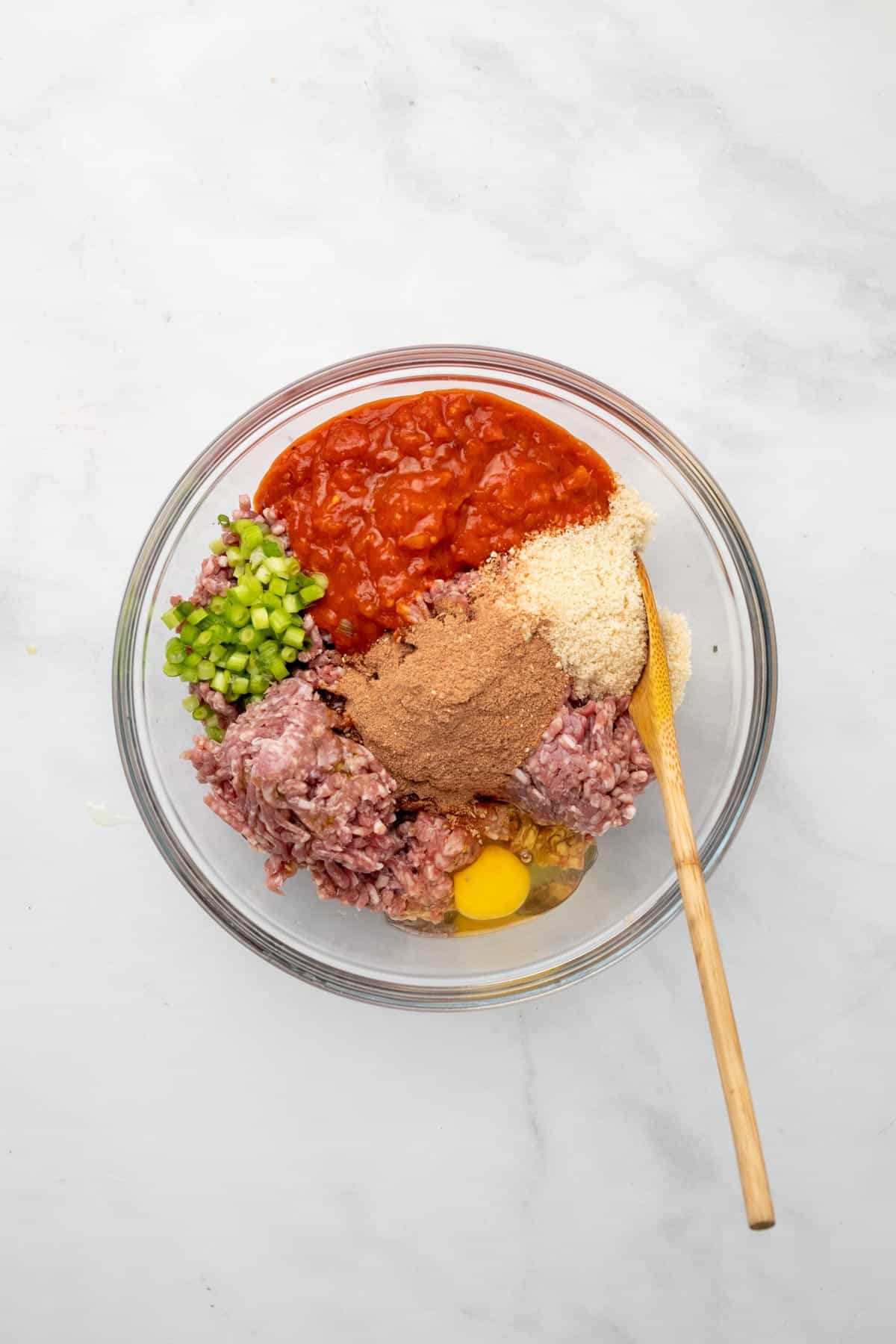 Meatloaf ingredients in a glass bowl with a wooden spoon, unmixed