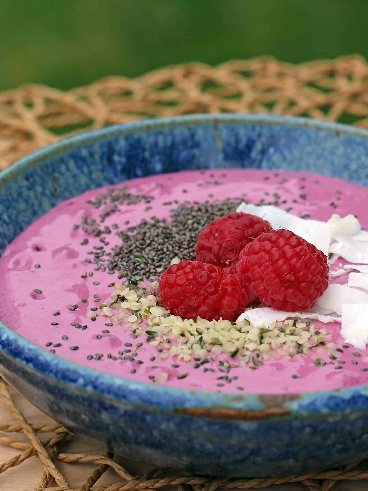 Berry Smoothie Bowl topped with chia seeds, hemp hearts, raspberries, and coconut flakes in a blue bowl