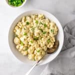 Cauliflower potato salad in a white bowl with a spoon, garnished with fresh green onion