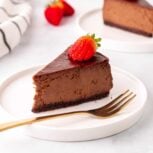 Low carb chocolate cheesecake slice on a white plate next to a gold fork, topped with a sliced strawberry