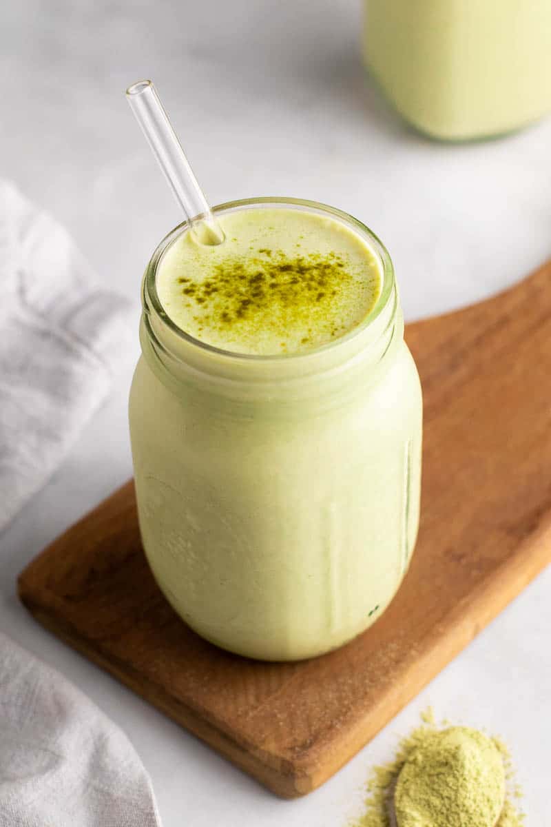 Smoothie in a glass jar with a straw, garnished with fresh matcha powder