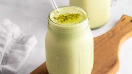 Matcha smoothie in a glass jar with a straw and matcha powder sprinkled on top