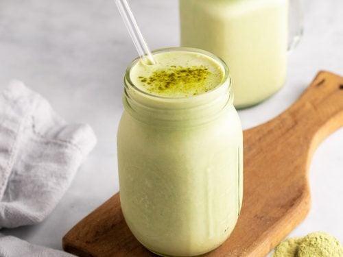 Matcha smoothie in a glass jar with a straw and matcha powder sprinkled on top
