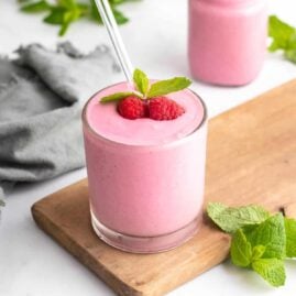 Raspberry smoothie in a glass on a wooden board, topped with fresh raspberries