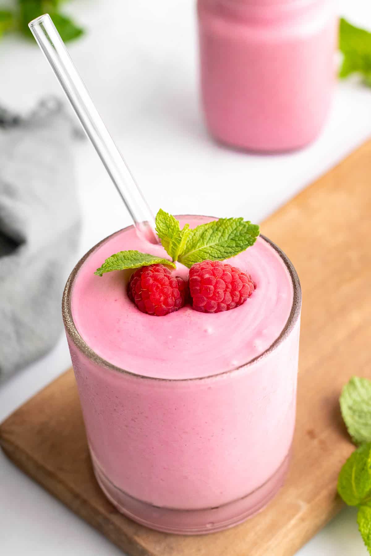 Raspberry smoothie in a glass jar on a wooden board, topped with fresh strawberries