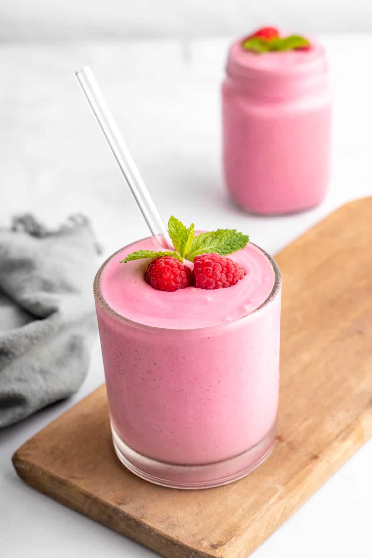 Smoothie in a glass jar with a straw, garnished with fresh raspberries