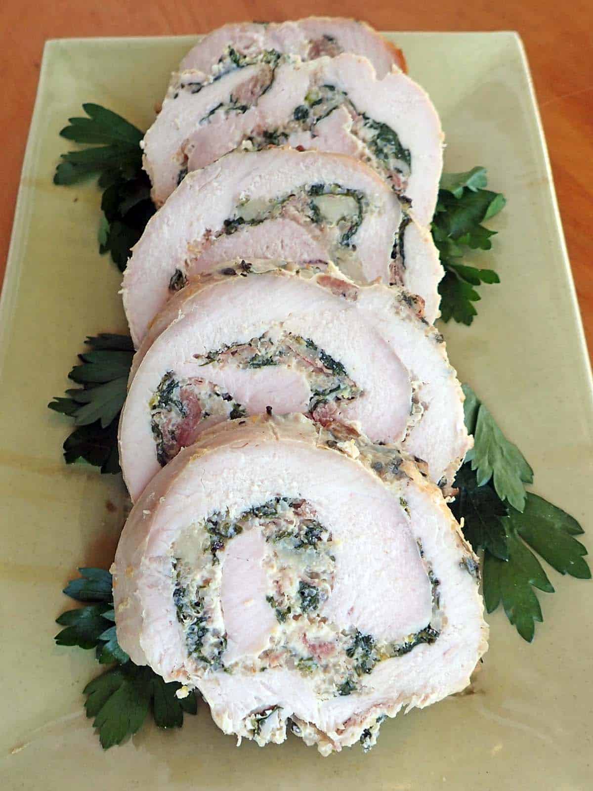 Turkey Roulade with Quinoa, Swiss Chard and Prosciutto cut into slices on a serving plate with parsley