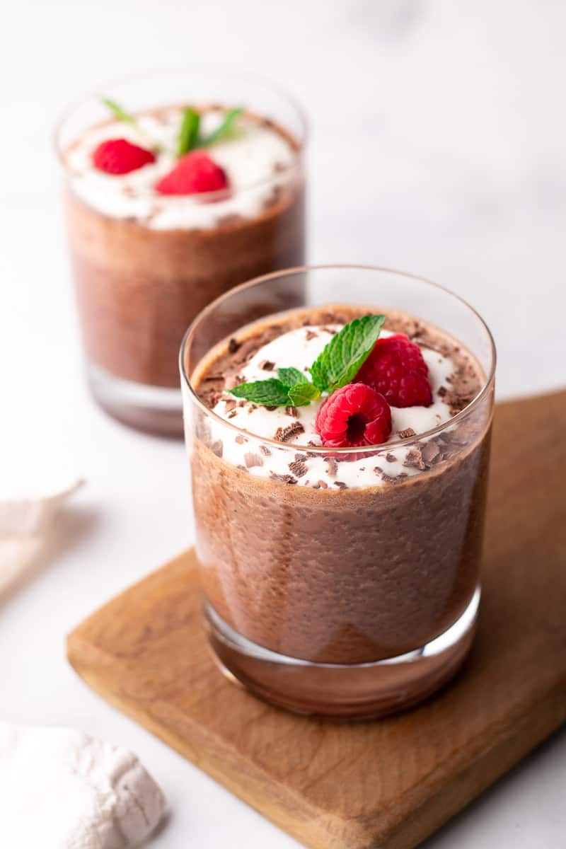 Pudding in a glass garnished with whipped cream, chocolate shavings, mint, and raspberries