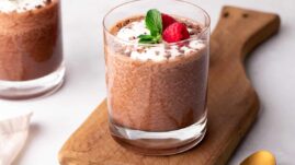 Keto chia pudding in a glass garnished with whipped cream, chocolate shavings, mint, and raspberries