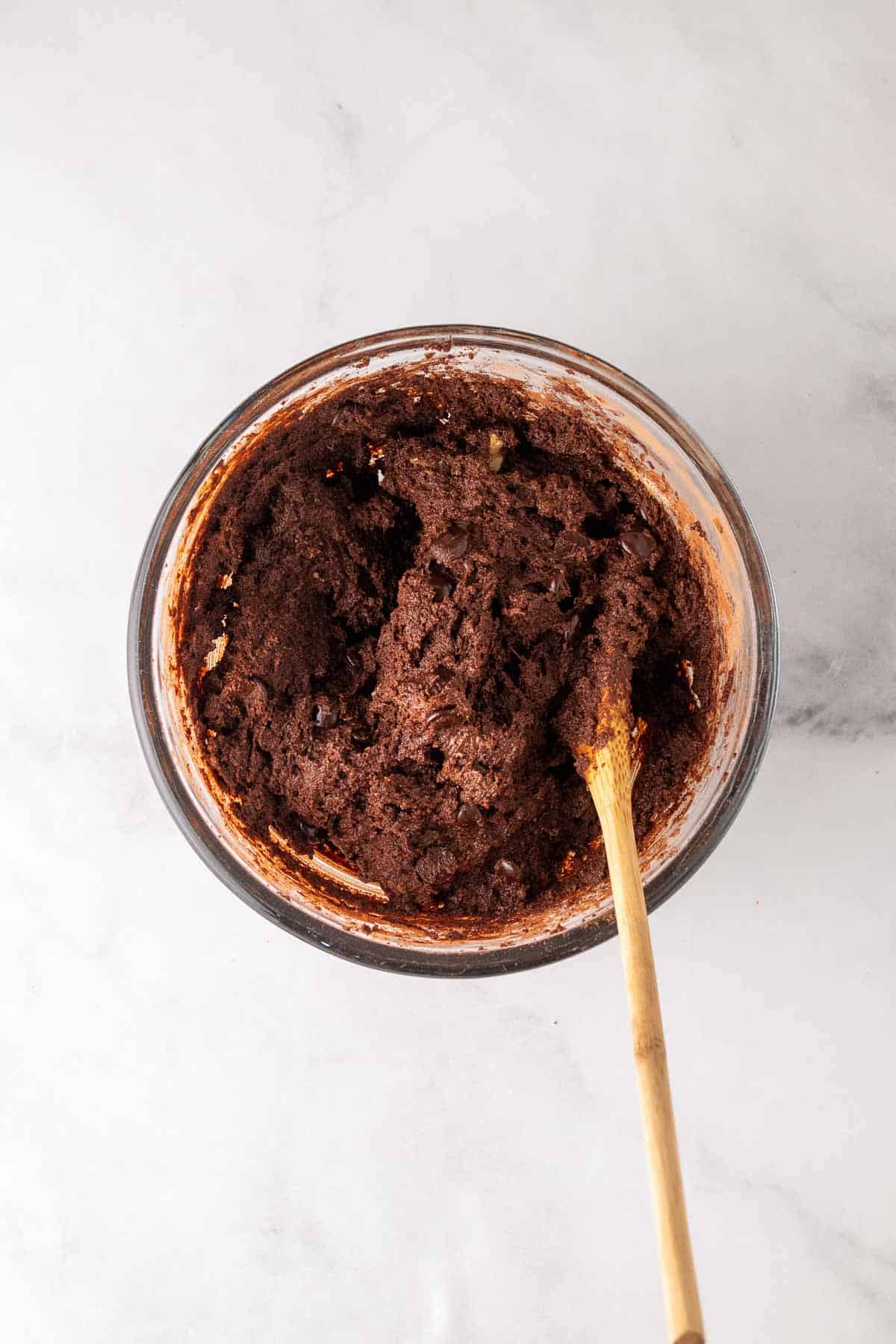 Brownie batter mixed together with a wooden spoon in a large glass bowl