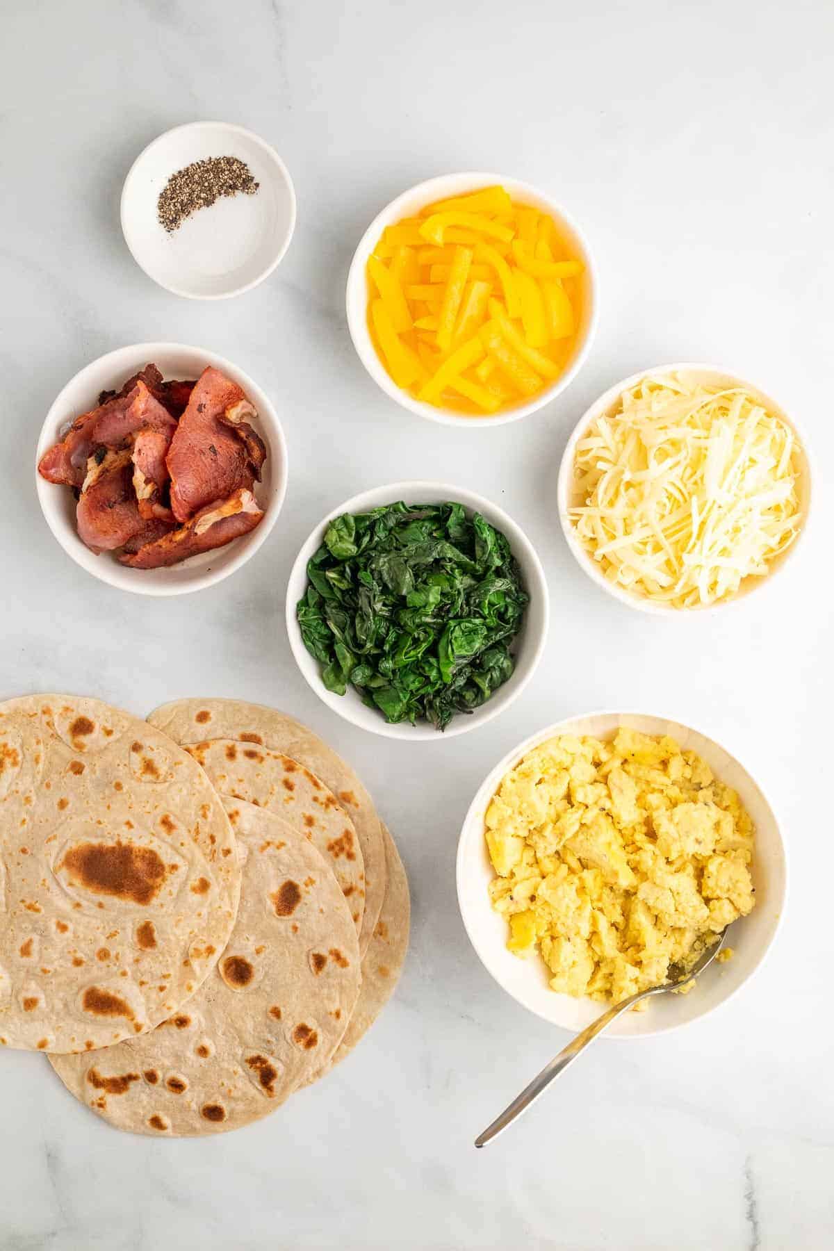 Individual burrito ingredients in separate ramekins and bowls, as seen from above