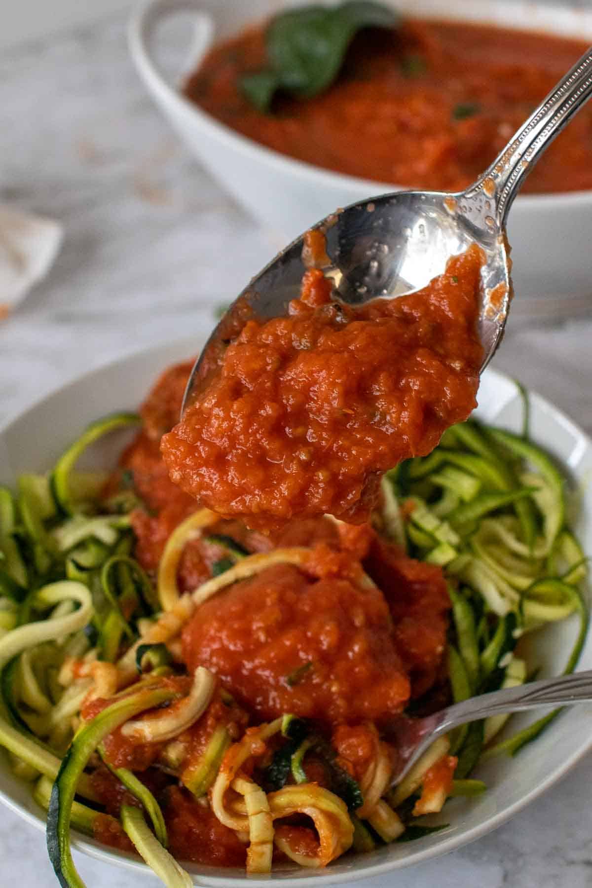 Spoonful of tomato sauce being put on vegetable noodles