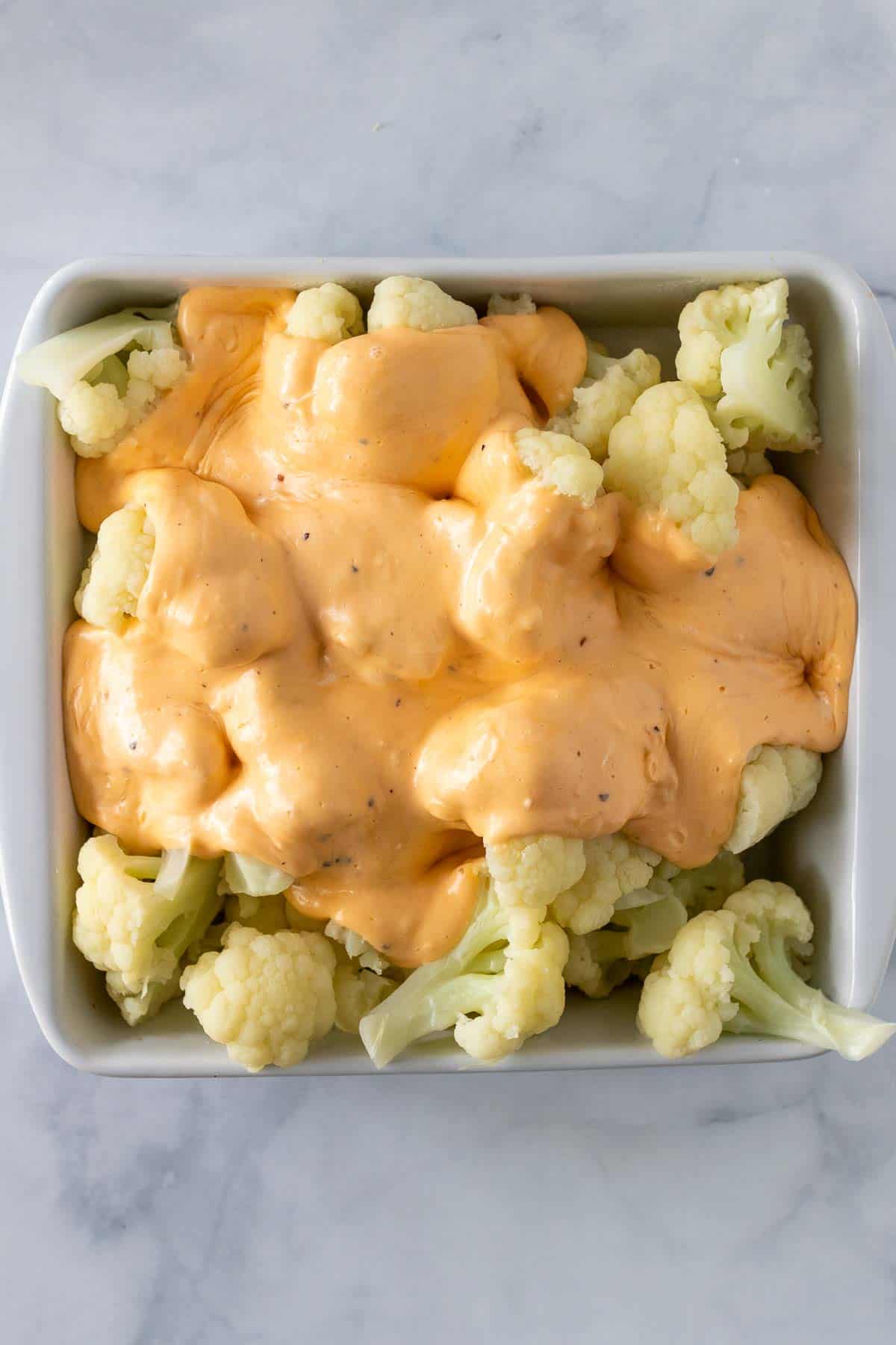 Cheese sauce poured over cauliflower in an 8x8 baking dish