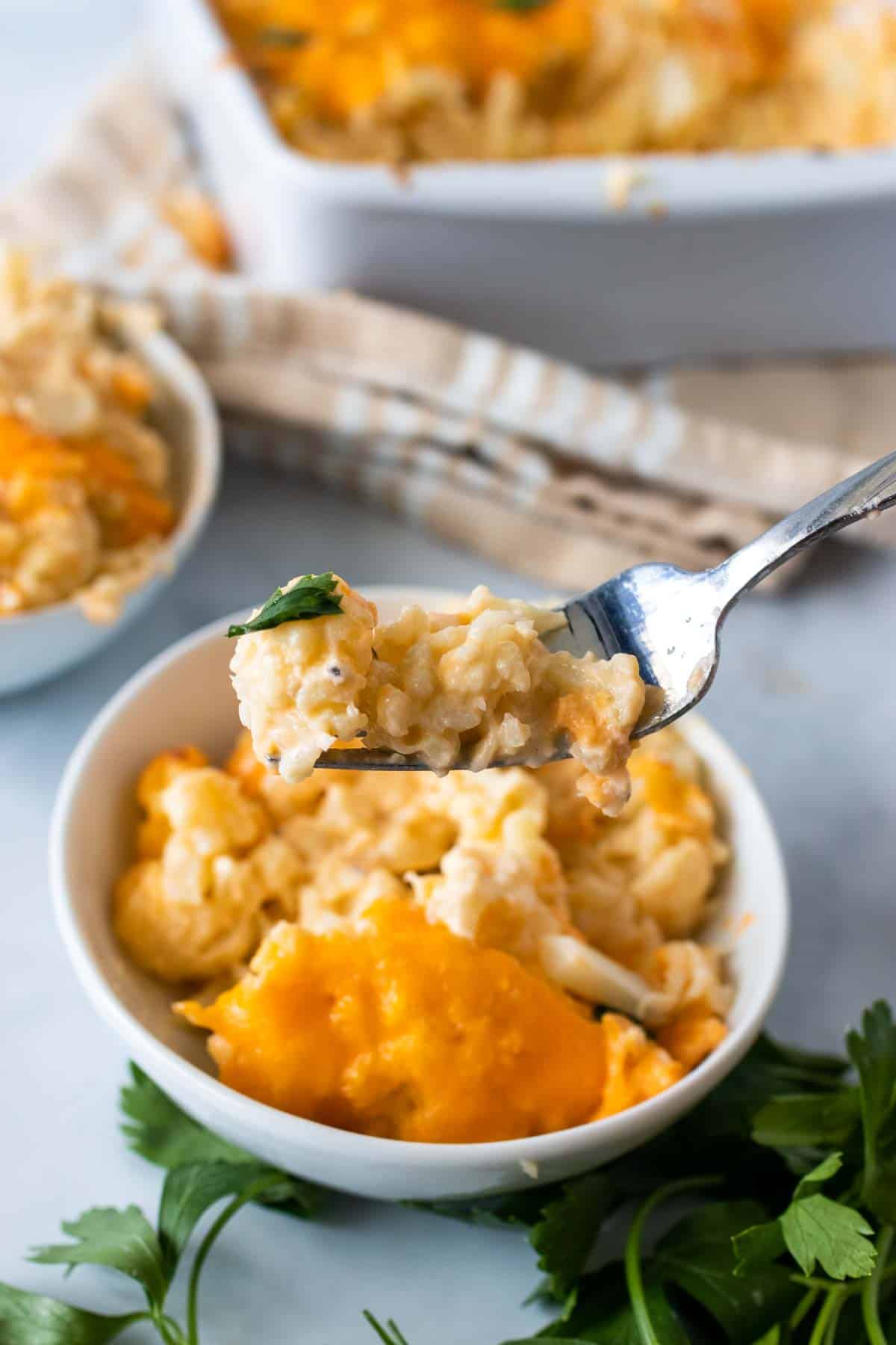 A forkful of cauliflower mac and cheese over the bowl with the full serving