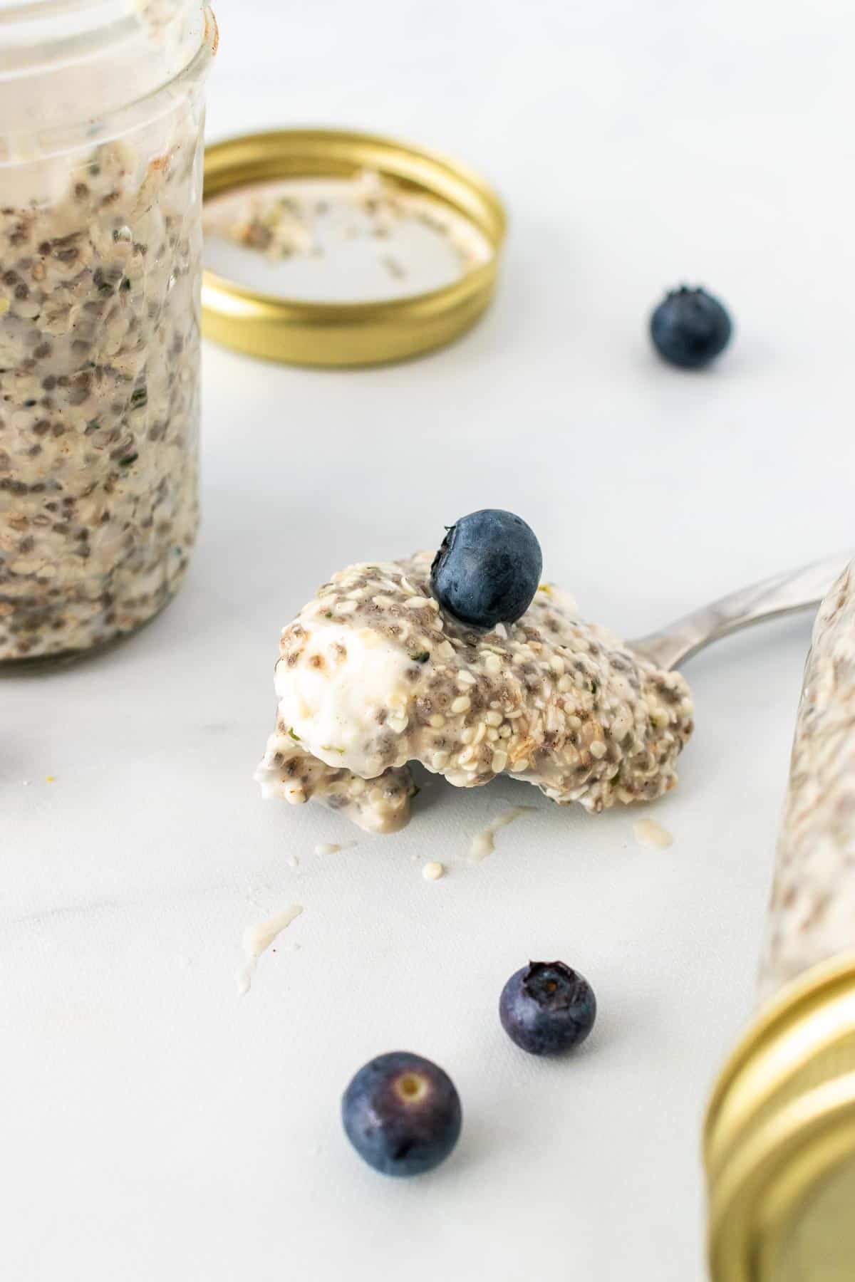 A spoonful of overnight faux oats with a blue berry on top next to an open jar of faux oats