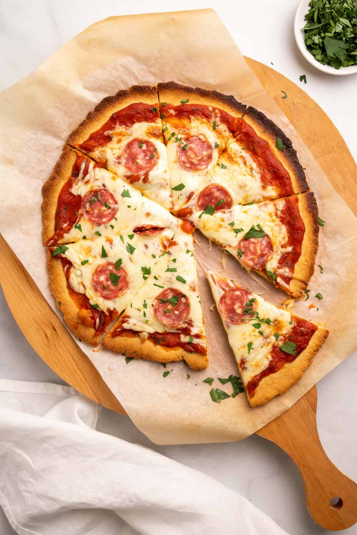Keto Pizza Crust topped with sauce, cheese, pepperoni, and fresh parsley, cut into slices with one slice slightly separated from the rest