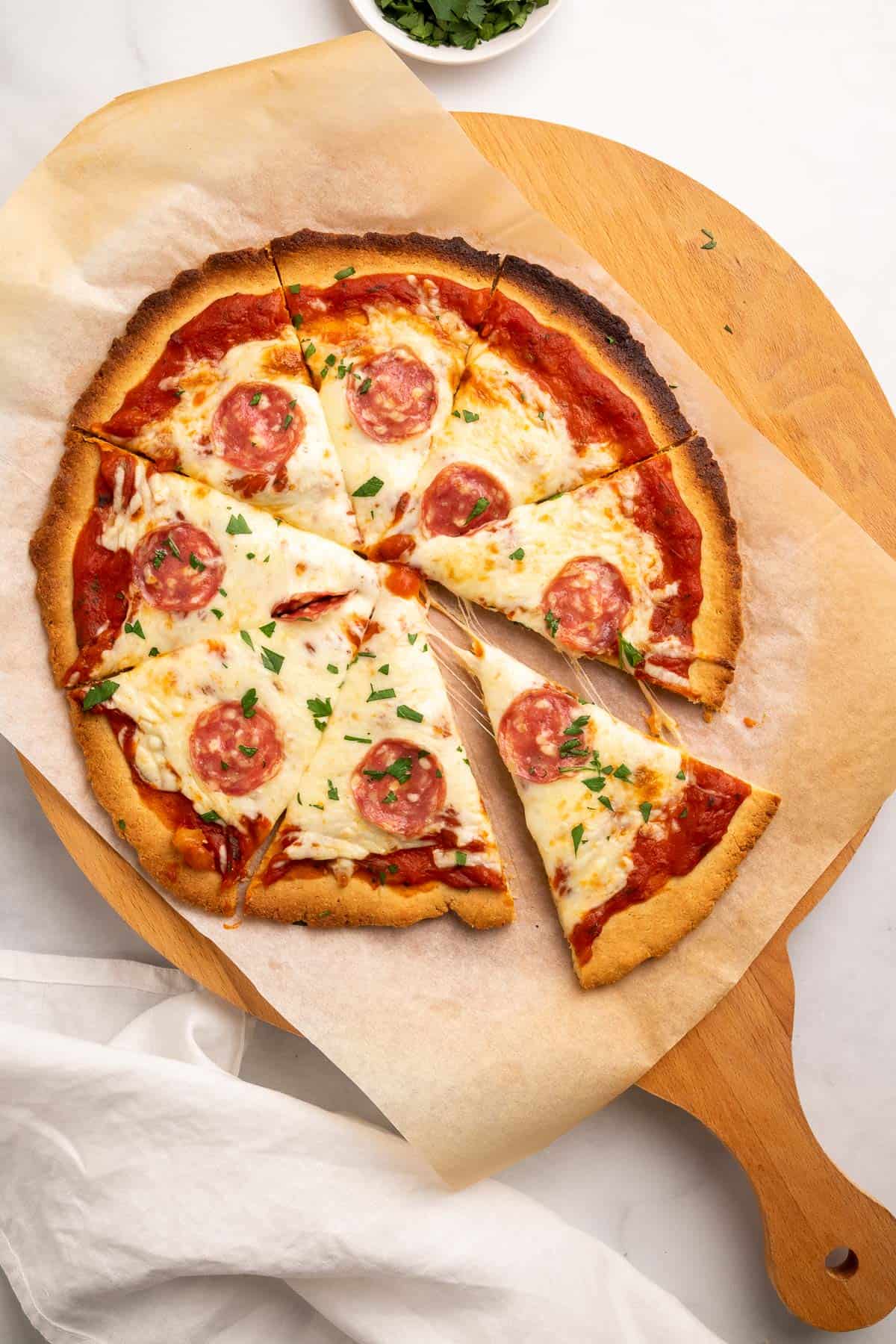 Pizza topped with sauce, cheese, pepperoni, and fresh parsley, cut into slices with one slice slightly separated from the rest
