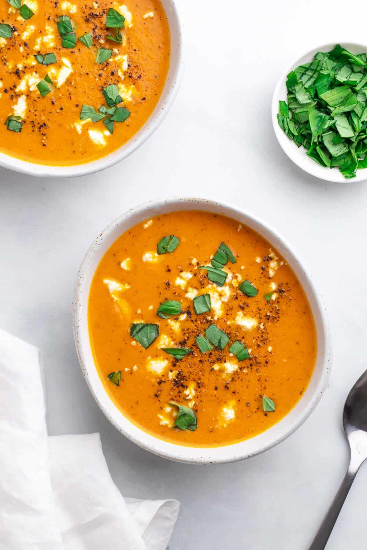Two bowls of Keto tomato soup topped with feta and garnished with fresh basil, as seen from above