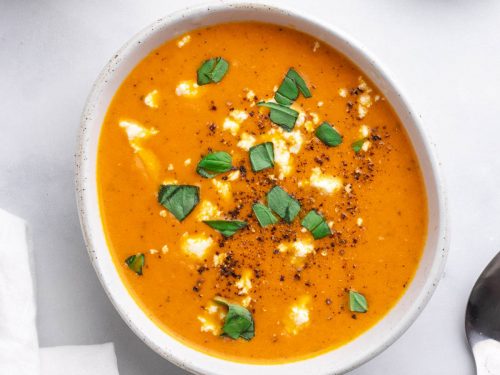 Keto tomato soup in a white bowl topped with feta and garnished with fresh basil, as seen from above
