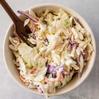 Low carb coleslaw in a white bowl with a wooden fork, as seen from above