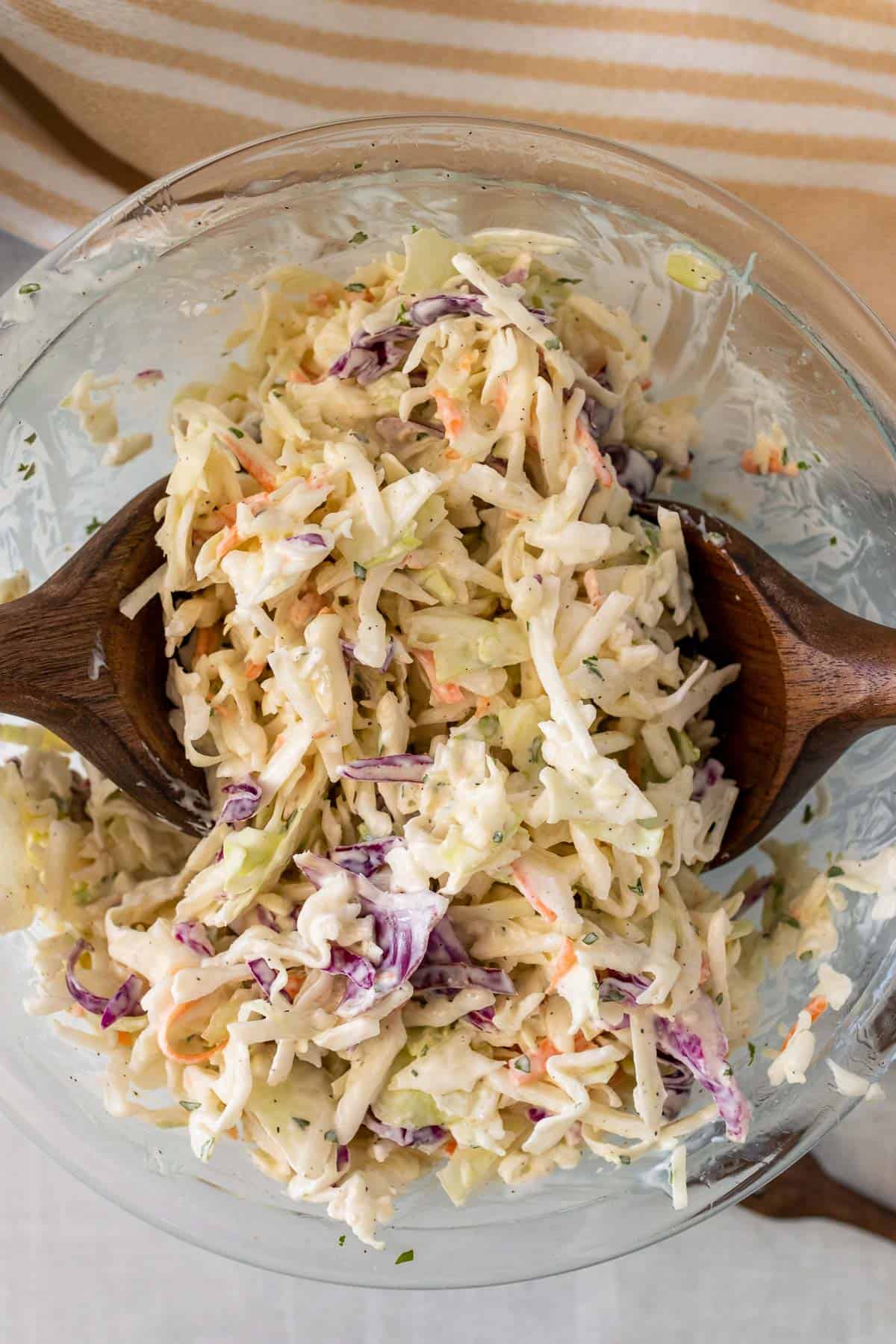 Coleslaw in a glass bowl being served with wooden serving utensils